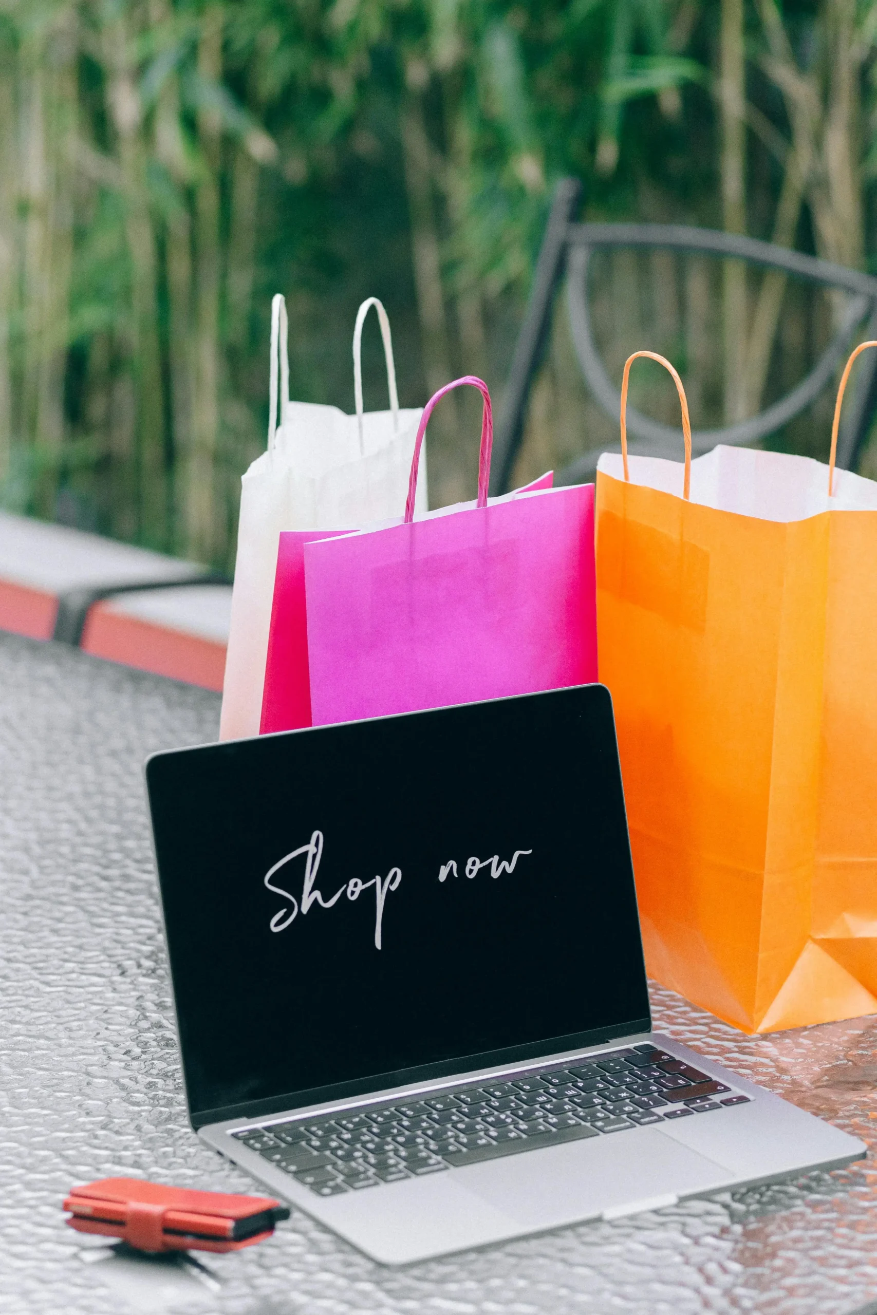 “Online shopping concept with colorful shopping bags and laptop displaying 'shop now' message”