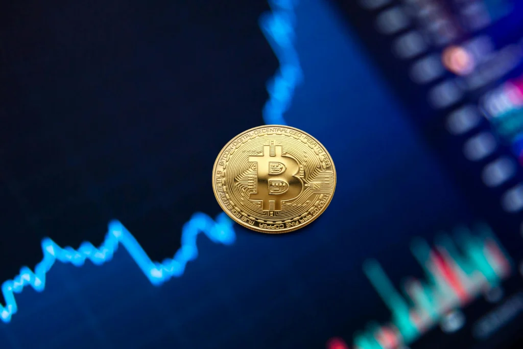 "A golden Bitcoin coin set against a digital screen showing fluctuating market graphs and candlestick charts, symbolizing cryptocurrency market trends."