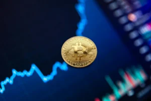 "A golden Bitcoin coin set against a digital screen showing fluctuating market graphs and candlestick charts, symbolizing cryptocurrency market trends."