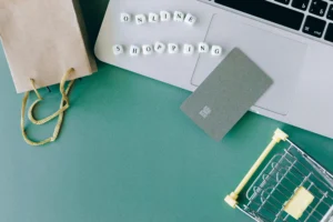 Flat lay of online shopping elements including a laptop, credit card, shopping bag, and mini cart, symbolizing e-commerce setup.