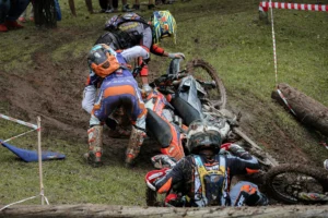 Motorcyclists involved in a muddy off-road crash with bikes and riders on the ground, illustrating the aftermath of a motorcycle accident.