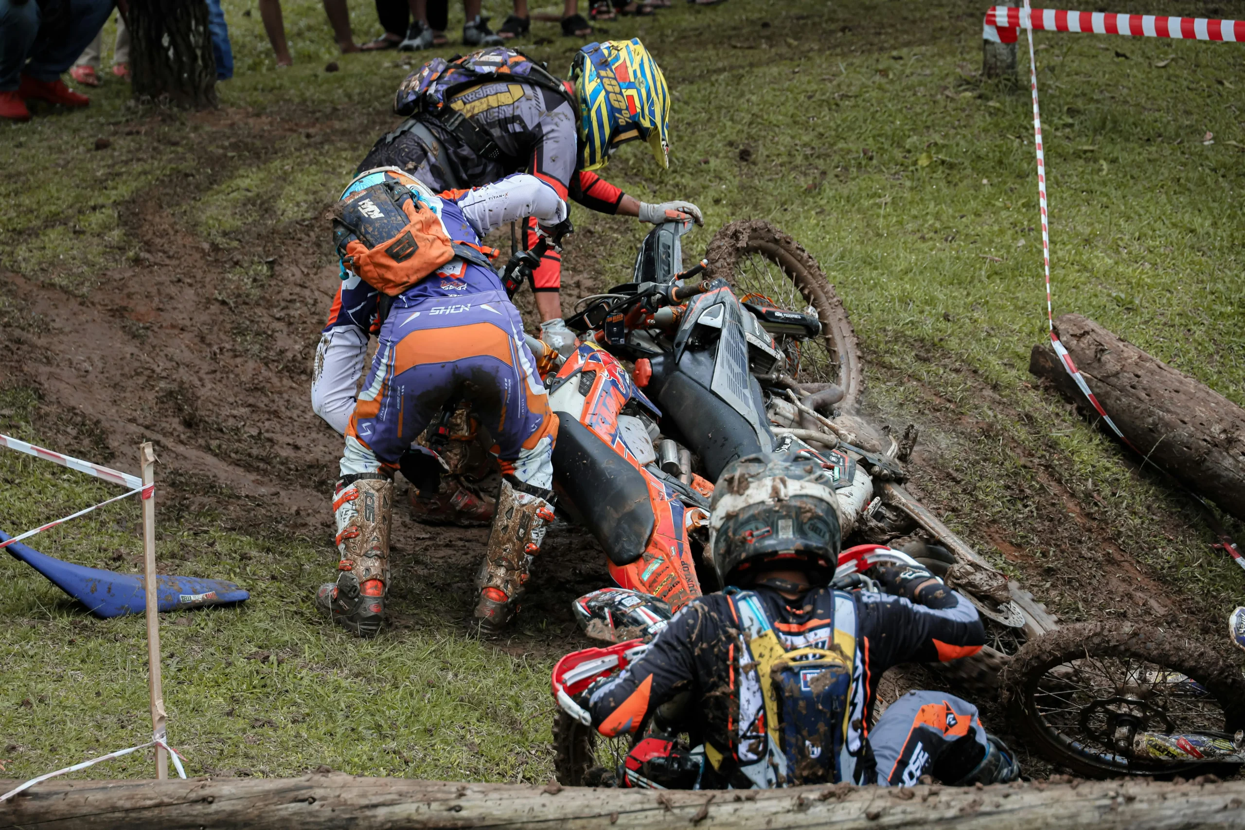 Motorcyclists involved in a muddy off-road crash with bikes and riders on the ground, illustrating the aftermath of a motorcycle accident.