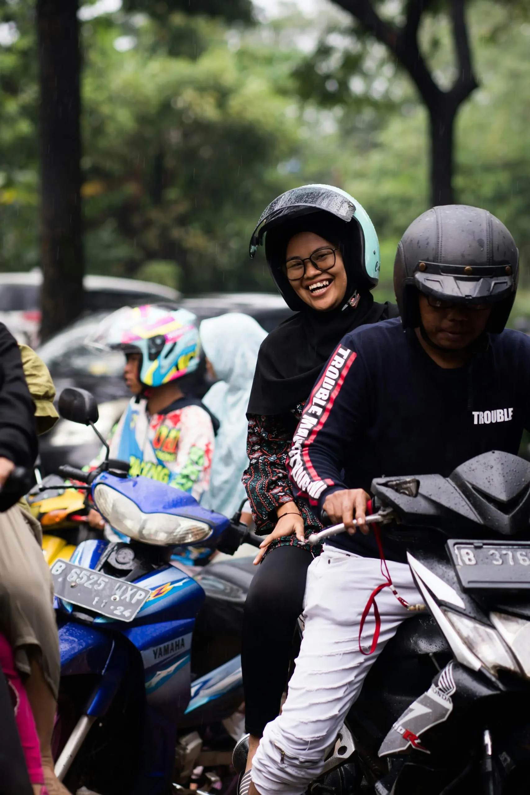 Group of motorcyclists in traffic, with one smiling passenger wearing a helmet, suggesting everyday riding conditions where insurance is crucial.