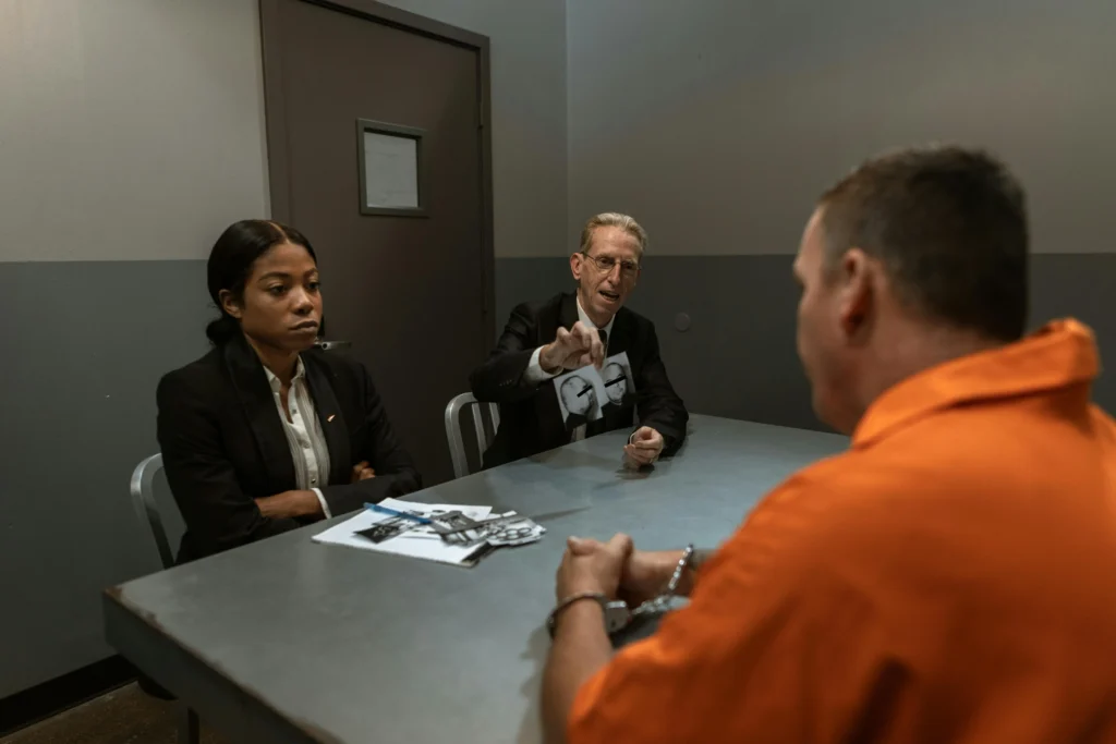 Lawyers in a serious discussion with a handcuffed man in an interrogation room, symbolizing legal strategies and defense in complex accident or insurance cases.