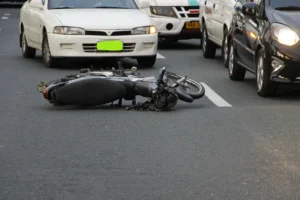 Motorcycle lying on the road after an accident surrounded by cars, highlighting differences in legal handling of motorcycle and car collisions.