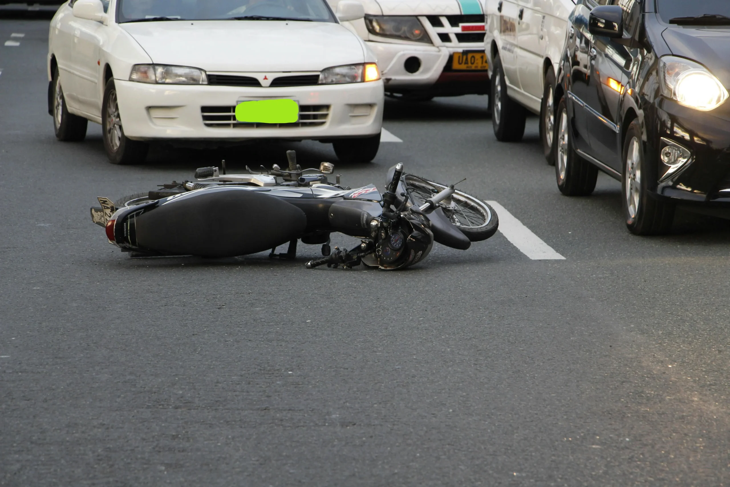 Motorcycle lying on the road after an accident surrounded by cars, highlighting differences in legal handling of motorcycle and car collisions.