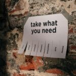 Paper sign on a brick wall with the message ‘take what you need,’ symbolizing essential guidance and preparation for professionals applying to work in Germany.
