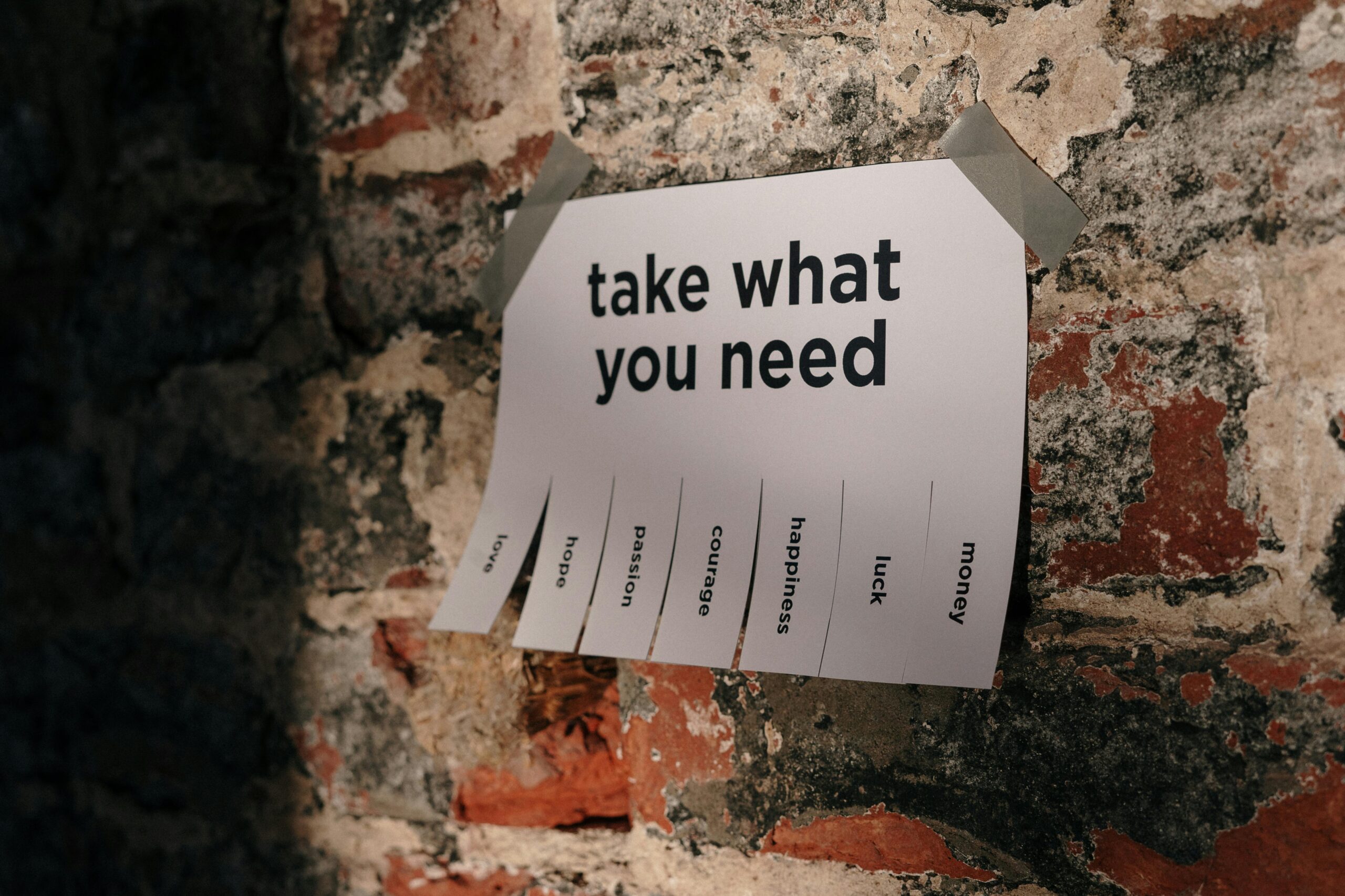 Paper sign on a brick wall with the message ‘take what you need,’ symbolizing essential guidance and preparation for professionals applying to work in Germany.