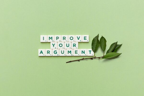 Scrabble tiles spelling “Improve Your Argument” with green leaves, symbolizing better preparation for immigration approval.