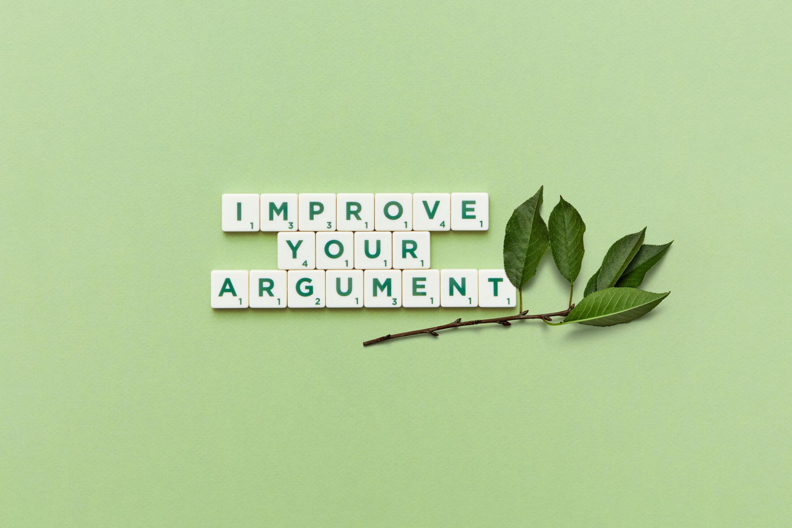 Scrabble tiles spelling “Improve Your Argument” with green leaves, symbolizing better preparation for immigration approval.